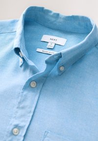 Camicia azzurro chiaro in cotone con bottoni, colletto appuntito, vestibilità regolare, con due bottoni frontali e taschino sul petto a sinistra.