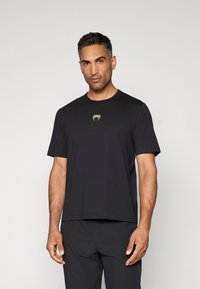 Sort kortærmet t-shirt lavet af blødt stof, med et centreret guld logo på brystet og en afslappet pasform.