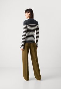 Haut à rayures à manches longues en marine et crème, texture côtelée, associé à un pantalon taille haute olive. Modèle vu de dos sur fond uni.