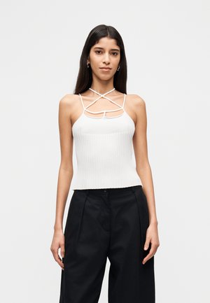 Top bianco a coste con design a incrocio sul collo e dettaglio a ritaglio, abbinato a pantaloni larghi neri. Texture liscia e forma aderente.