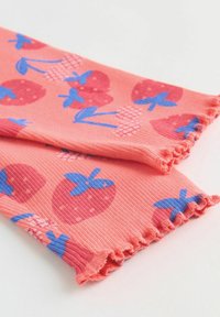 Tissu côtelé rose corail avec des motifs de fraises bleues et rouges et des bords froncés, présenté plié sur une surface blanche.