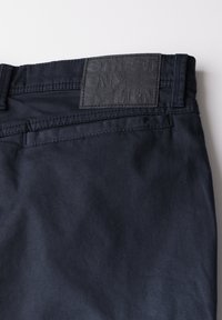 Navy blue trousers made of cotton with a textured finish, featuring a leather logo patch on the waistband and a practical back pocket.