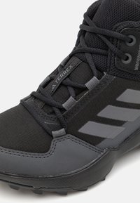 Black hiking shoe with textured fabric upper, reinforced rubber toe, and grey accents. Features prominent lacing and three grey stripes.