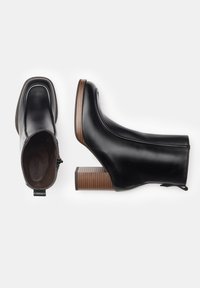 Black leather ankle boots with a square toe, side zipper, and a brown striped block heel. Smooth texture with minimalistic design details.