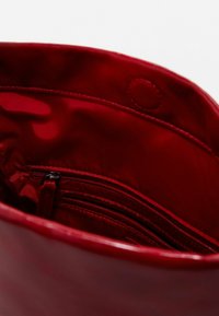 Rotes synthetisches Handtascheninnere mit glänzender Textur, ausgestattet mit einer Tasche mit Reißverschluss und zusätzlichen Fächern zur Organisation.