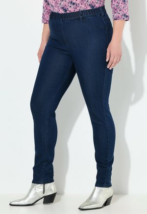 Tummansiniset venyvät farkut, joissa on joustava vyötärö, etutaskut ja kapea istuvuus. Yhdistettynä metallinhohtoisiin hopeisiin korkokenkiin.