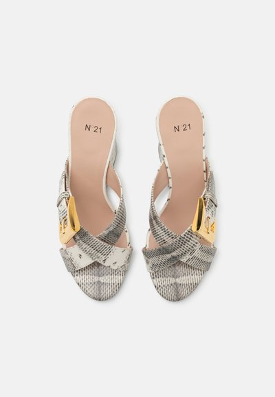 Sandales à talons avec un design à lanière croisée en imprimé serpent neutre, présentées avec une boucle dorée et une semelle douce beige.