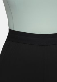 Zwarte sportieve broeken met een brede, gladde zwarte tailleband; gecombineerd met een licht muntgroene, gestructureerde top. De nadruk ligt op eenvoud en comfort.