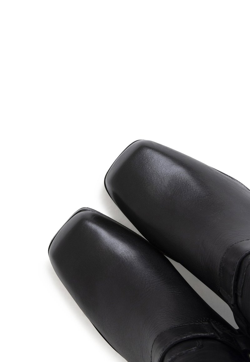 Bottines en cuir noir avec un bout carré et une texture lisse, présentant un design minimaliste sans matériel ni accents visibles.