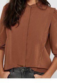 Braune, leichte Bluse mit rundem Kragen, kurzen Puffärmeln und Vorderfalten. Glatte Textur mit einem leicht lockeren Schnitt.