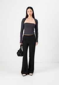 Σκούρος γκρι μακρυμάνικος τοπ με σχεδίαση strapless, συνδυασμένο με μαύρα φαρδιά παντελόνια. Μαύρη τσάντα χειρός με λουλουδάτο σχέδιο, μπεζ παπούτσια.