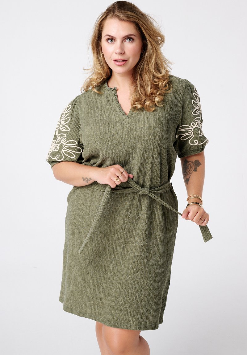 Olijfgroene jurk van textuurstof, met V-hals en geborduurde korte mouwen. Inclusief een bijpassende riem die om de taille is geknoopt.
