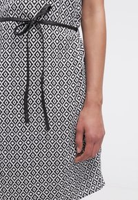 Svartvit mönstrad klänning med en diamantdesign, med ett svart bälte i midjan och en rak nederkant.