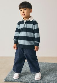 Polo de manga larga a rayas en marino y azul clara con cuello blanco, combinado con pantalones vaqueros oscuros y anchos y zapatillas blancas. Alfombra texturizada debajo.