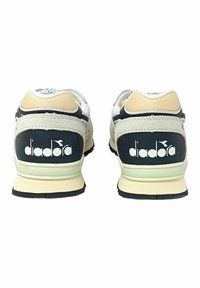 Sneaker bianche e blu navy con accenti beige, dotate di una tomaia in mesh testurizzato, colletto imbottito e un prominente logo Diadora sul tallone.