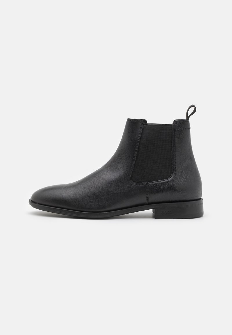 Botín Chelsea de cuero negro con panel lateral elástico, lengüeta en el talón y tacón bajo apilado sobre fondo blanco.