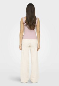 Top de tirantes ajustado en color rosa con bordes de volantes, combinado con pantalones anchos blancos con bolsillos traseros, visto desde la espalda.