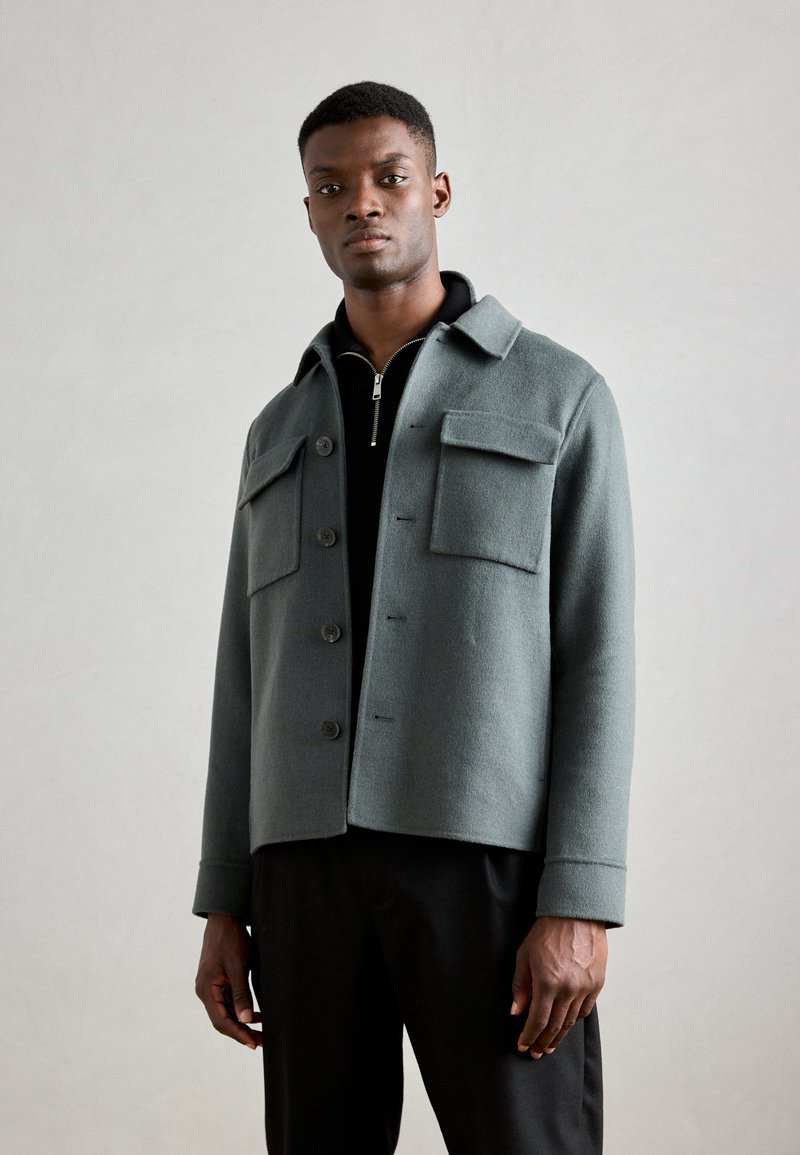 Gray wool blend jacket with a collared neckline, front buttons, and two chest pockets. Smooth texture and tailored fit.