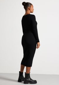 Sort ribbede langærmede kjole med en tætsiddende silhuet, knælang, med bølget kant, parret med sorte kraftige ankelstøvler.