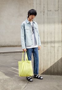 Chaqueta de mezclilla azul clara, camiseta gráfica, jeans azules, sandalias negras y una bolsa de mano amarilla. Texturas suaves, corte holgado, estilo casual.
