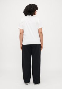 Witte T-shirt met korte mouwen, gecombineerd met losse zwarte broeken. Glad materiaal, eenvoudig ontwerp, rechte zoom en relaxte pasvorm.