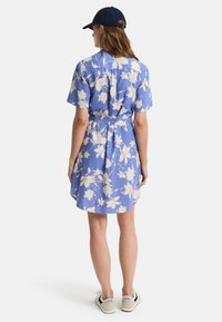 Blå blomstret kjole med korte ermer, belte i midjen og lyse blomster. Myk stoff og avslappet passform. Brukt med en mørk caps og joggesko.