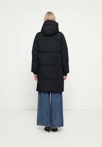Schwarze Pufferjacke mit Kapuze, im gesteppten Design und langen Ärmeln, kombiniert mit weiten blauen Jeans.