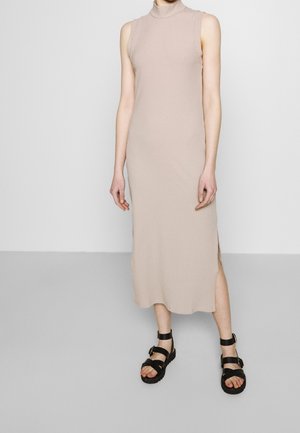 Abito midi beige a coste senza maniche con collo alto; presenta spacchi laterali. Abbinato a sandali neri con cinturini e fibbie.