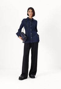 Laivastonsininen farkkupaita napit edessä, pitkät hihat ja leveät hihansuut, yhdistettynä löysiin mustiin housuihin ja mustaan käsilaukkuun. Pehmeät pinnat kauttaaltaan.