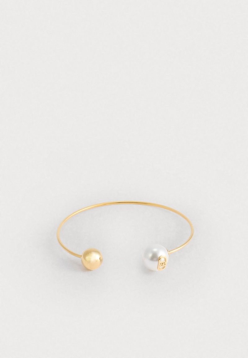 Bracciale a maniche in tono oro che presenta una perla dorata e una perla bianca a ciascun estremo, con un design minimale e liscio e una forma circolare e aperta.