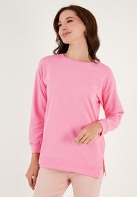 Felpa rosa con maniche lunghe, collo rotondo e aperture laterali. Il tessuto appare liscio e ha una vestibilità rilassata. Adatta per abbigliamento casual.