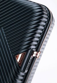 Black suitcase with vertical ribbed design, rose gold hardware, a triangular logo plate, and a dual zipper closure. Textured surface.