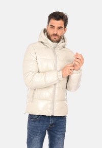 Giacca puffer imbottita di colore crema chiaro con finitura lucida, cappuccio e zip frontale. Presenta polsini a costine e una silhouette adatta.