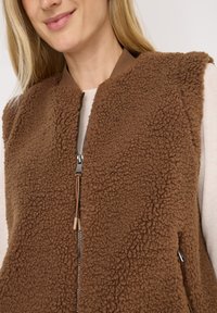 Brown fleece vest with a textured surface, featuring a front zipper and elasticized cuffs. The design is unlined with side pockets.