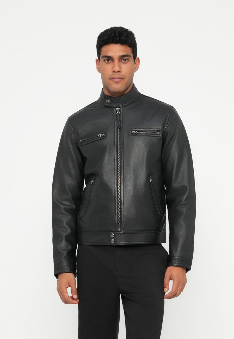 Juodas odinis švarkas su stovinčiu apykaklės kraštu, priekyje užtrauktuku, ir keturiais užtrauktukais uždaromais kišeniais; lygus paviršius ir prigludusi forma.