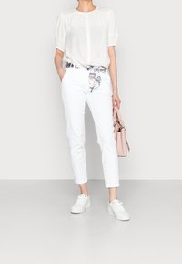 White blouse with puffed sleeves, white tailored pants, and a floral patterned belt. Paired with white sneakers and a light pink handbag.