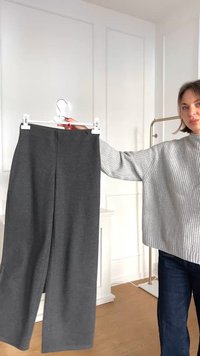 Sive visoke hlače izrađene od meke tkanine s opuštenim krojem, s glatkom teksturom i minimalnim detaljima.