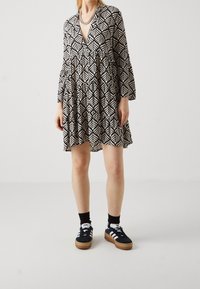 Vestido de patrones en blanco y negro con mangas acampanadas, escote en V y diseño en capas. Combinado con zapatillas en blanco y negro y calcetines negros.
