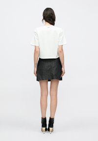 Biała krótka koszulka z krótkimi rękawami, zestawiona z ciemnoniebieską mini spódnicą z denimu. Czarne botki za kostkę z ostrym noskiem i jasnokolorowymi obcasami.