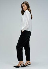 Blouse blanche légère à manches longues avec des poignets froncés, associée à un jean noir tapered taille haute et des escarpins à talons ouverts noirs.