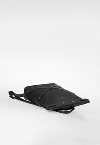 Schwarzer rechteckiger Rucksack liegt flach, mit verstellbaren Gurten, einem oberen Griff und einer diagonalen Reißverschlusstasche vorne.