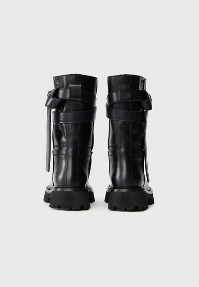 Juodas odinis batus su aukštu aulu, storomis juodomis guminėmis padangomis ir keliais dirželiais. Lygus paviršius su matomomis siūlėmis.