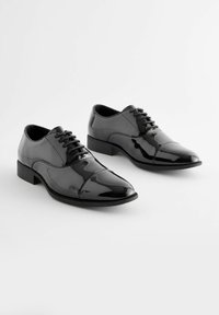 Schwarze Lackleder-Dress-Schuhe mit spitz zulaufender Zehe, Schnürdesign und niedrigem Absatz. Glatte Oberfläche mit leichtem Glanz.