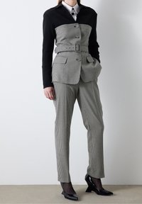 Conjunto a medida con un patrón de pata de gallo en blanco y negro, blazers estructurado con cintura ceñida y pantalones ajustados. Tacones de charol negros.