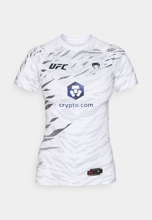 Balta trumpų rankovių sportinė marškinė su geometriniu raštu. Su UFC logotipu, mėlynu heksagono grafiku su tekstu "crypto.com" ir juodais akcentais.