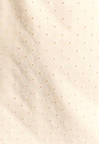 Witte stof met een ruitpatroon en kleine uitsparingen, met textuurdetails die een lichte uitstraling creëren.