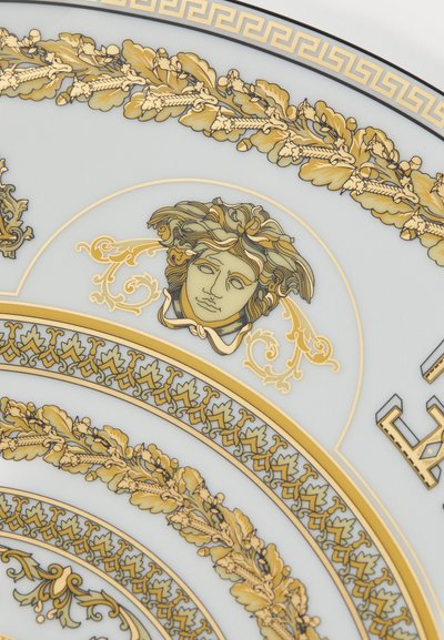 Talerz dekoracyjny z jasnoniebieskim tłem, złotymi i czarnymi akcentami, zawierający misterny wzór liści oraz centralny motyw twarzy w kolorze złotym.