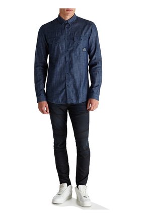 Granatowa koszula na guziki o fakturowanym splocie, z dwoma kieszeniami na piersi i małym logo, zestawiona z dopasowanymi czarnymi spodniami i białymi tenisówkami.