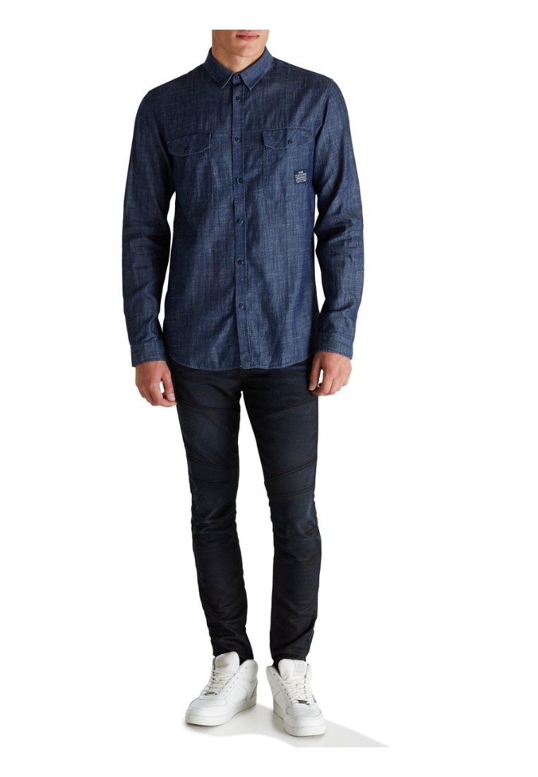Granatowa koszula na guziki o fakturowanym splocie, z dwoma kieszeniami na piersi i małym logo, zestawiona z dopasowanymi czarnymi spodniami i białymi tenisówkami.