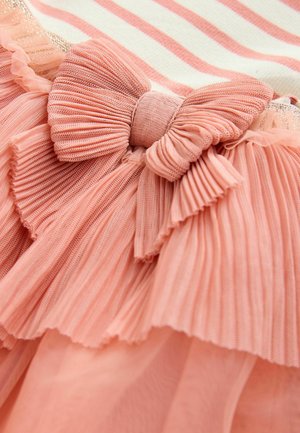 Détail d'une robe à volants en tissu plissé corail, avec un grand nœud en accent et un motif rayé subtil dans une palette de couleurs crème et corail.